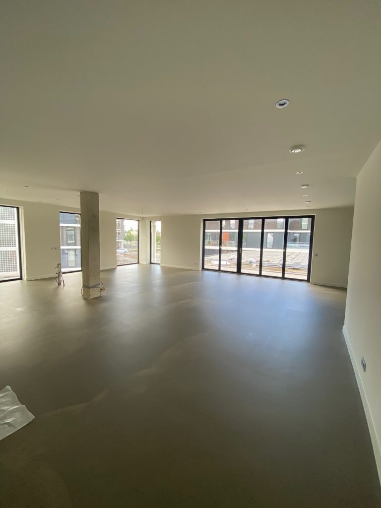 Lege nieuwbouw woonkamer met betonvloer en strak gestucte wanden en plafonds, klaar voor airless latex spuiten door De VerfBroeders
