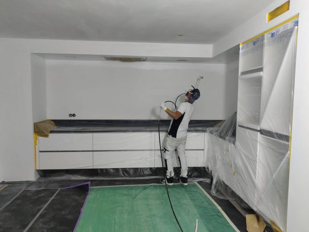 Schilder van De VerfBroeders voert airless latex spuiten uit op een plafond in een keuken, alles zorgvuldig afgeplakt met folie en tape voor een stofvrij en strak resultaat